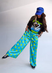 Person wearing a black t-shirt with a graphic design, blue cap, and bright blue pants with green polka dots on a white background.